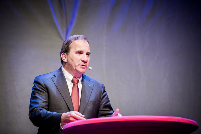 Stefan Löfven står i en talarstol. Han har kort hår, slips och en mikrofon vid munnen.