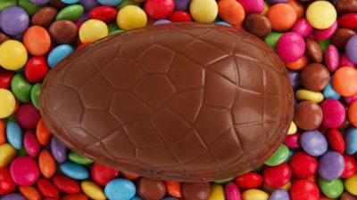 Ett stort chokladägg ligger på en bädd av färgglada chokladlinser.