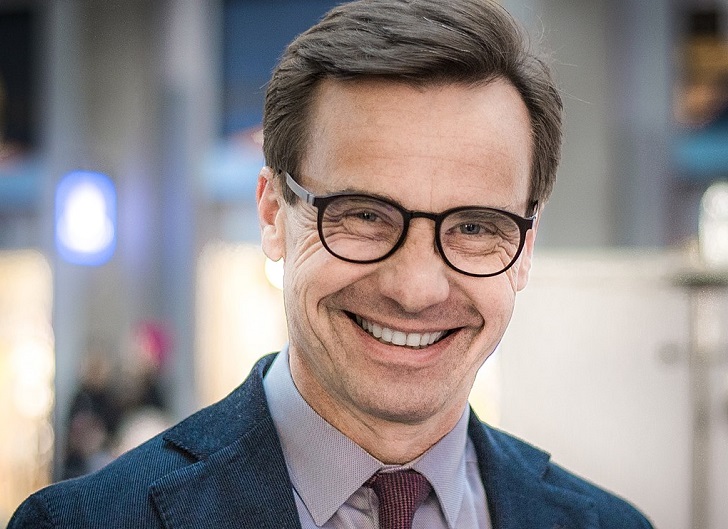 Ulf Kristersson har glasögon, kort hår och en kostym. Han har en del rynkor runt ögonen som syns extra mycket eftersom han ler stort.