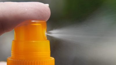 Bild på ett finger som trycker på en sprayflaska. Ut kommer solkräm.