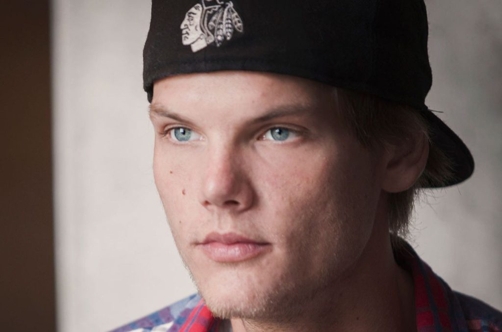 Porträttbild av Avicii. Han har rutig skjorta och en keps bakochfram. Han ser ut att vara ungefär 20 och ser allvarlig ut.